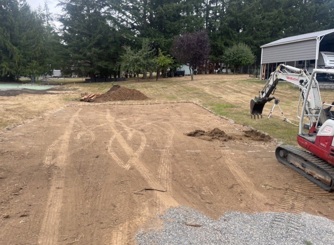 Excavator grading a cleared building pad ahead of a foundation